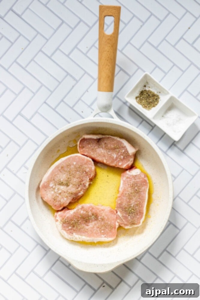 Perfectly Pan Fried Thin Pork Chops 7 Raw, seasoned pork chops being added to a hot skillet with olive oil, beginning the pan-frying process.