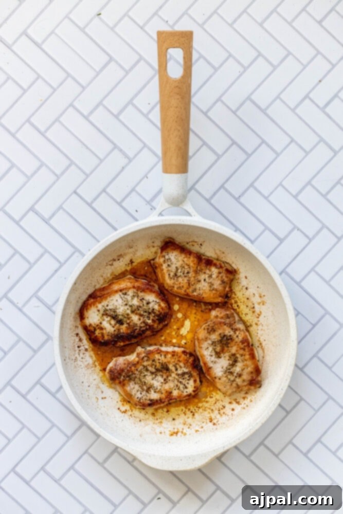 Perfectly Pan Fried Thin Pork Chops 8 Two beautifully browned pork chops searing in a hot skillet, with a golden crust forming on the edges.