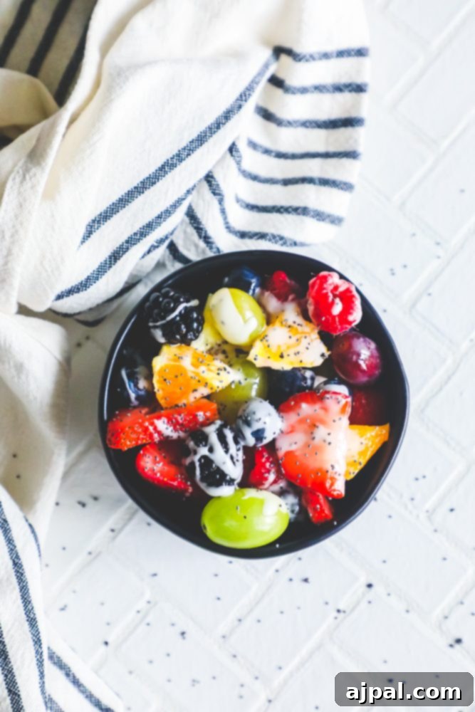 A beautiful bowl of fruit salad adorned with a glistening lemon poppyseed dressing, resting on a rustic wooden table.