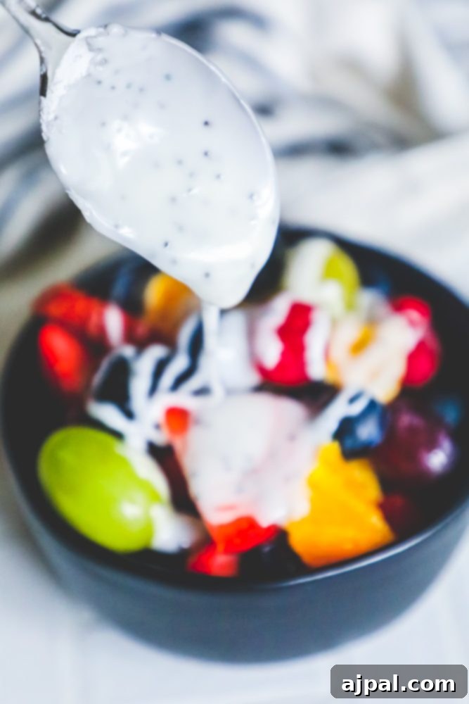 A spoon meticulously drizzles glistening lemon poppyseed glaze over a vibrant bowl of fresh fruit salad, highlighting the beautiful texture and sheen of the dressing.