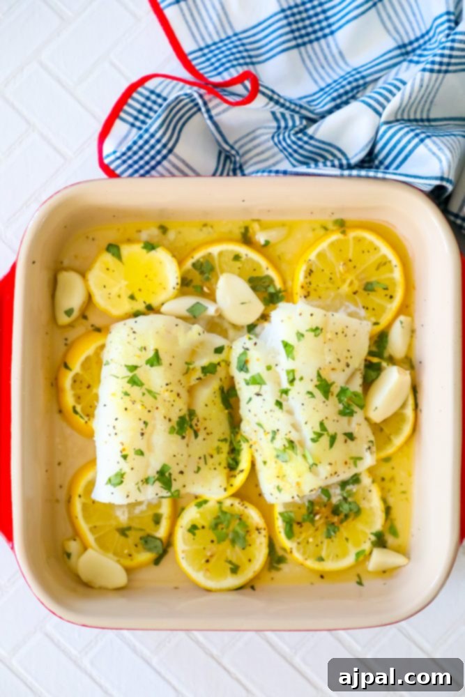 Lemony Garlic Baked Cod 4 picture of baked cod in a ceramic dish with lemon slices and garlic cloves in the dish