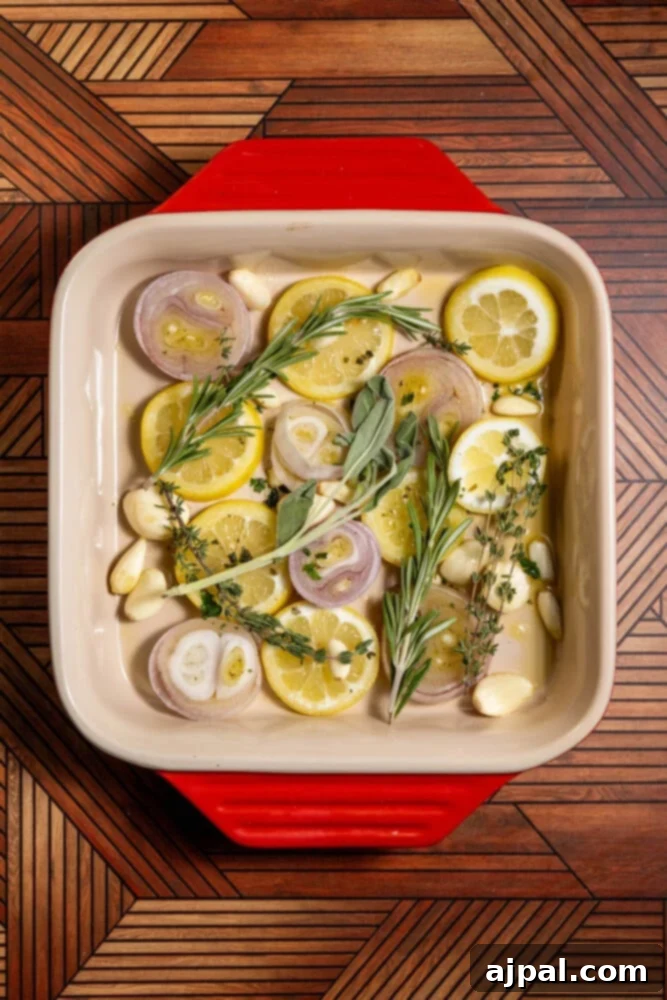 Slices of lemon, shallots, garlic cloves, and sprigs of fresh herbs in a baking dish, preparing for roasting.