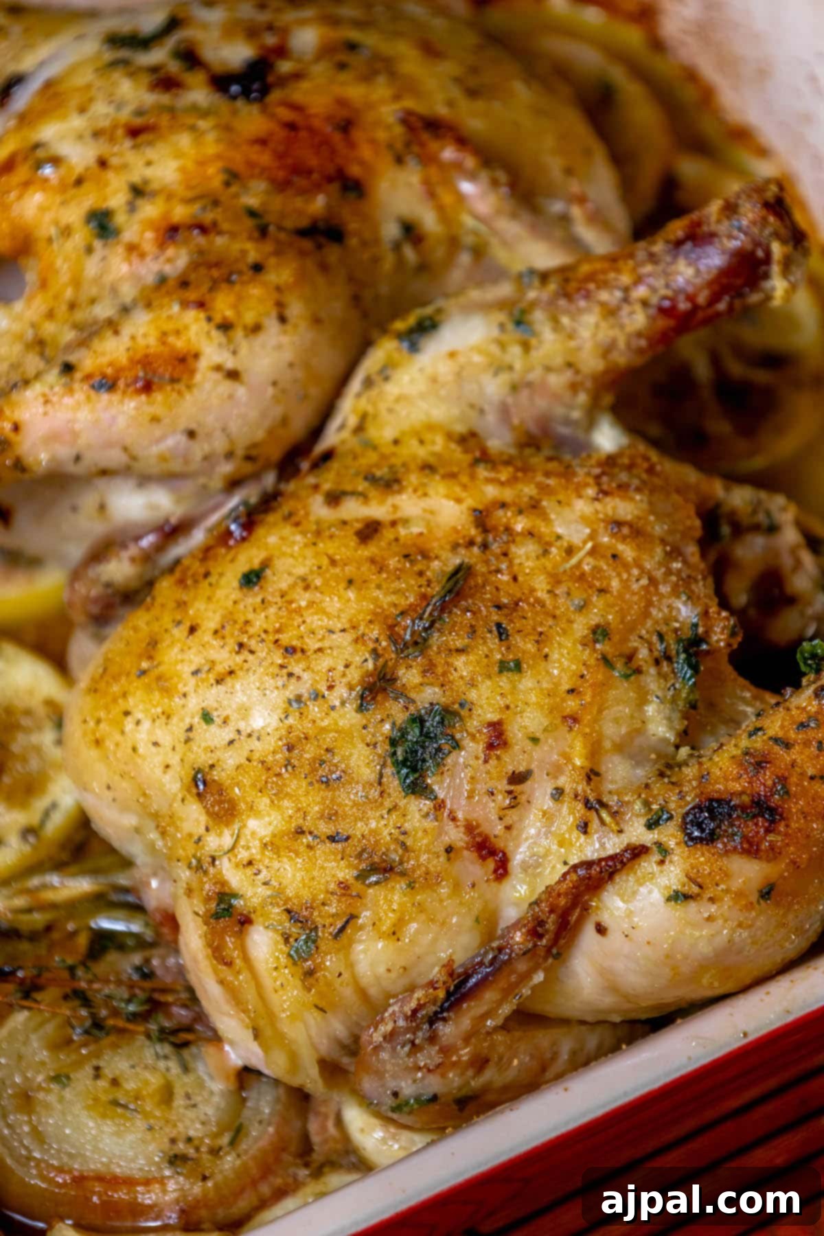 Crispy roasted Cornish game hen, beautifully browned, in a square baking dish alongside lemons, shallots, and garlic, ready for serving.