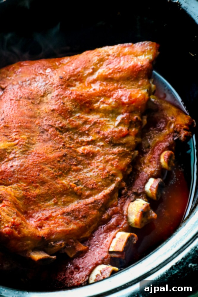 Easy Slow Cooker Ribs arranged in the slow cooker, ready for cooking.
