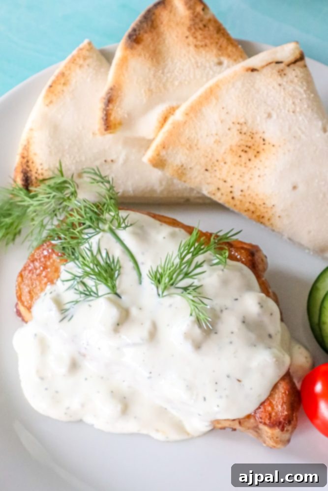 A beautifully plated baked Greek pork chop topped with creamy feta sauce, served with fresh herbs.