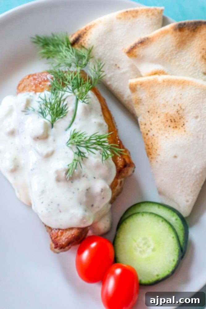 A plate featuring baked garlic pork chops with a generous dollop of creamy feta sauce, garnished with fresh tomatoes and cucumbers.