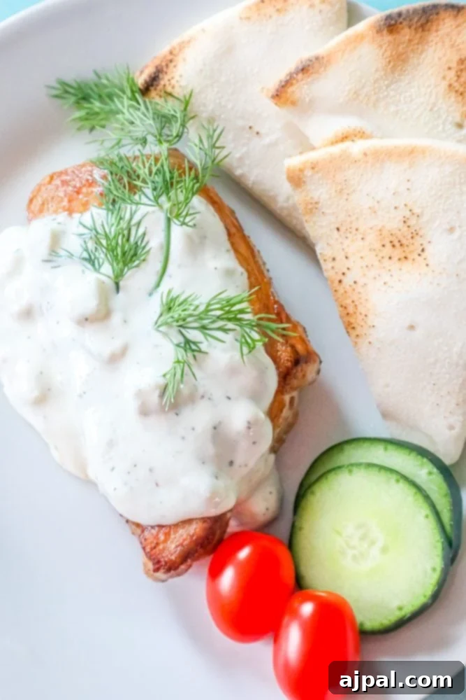 A savory pork chop generously coated in creamy feta sauce, accompanied by fresh cucumbers and tomatoes, artfully arranged on a plate.