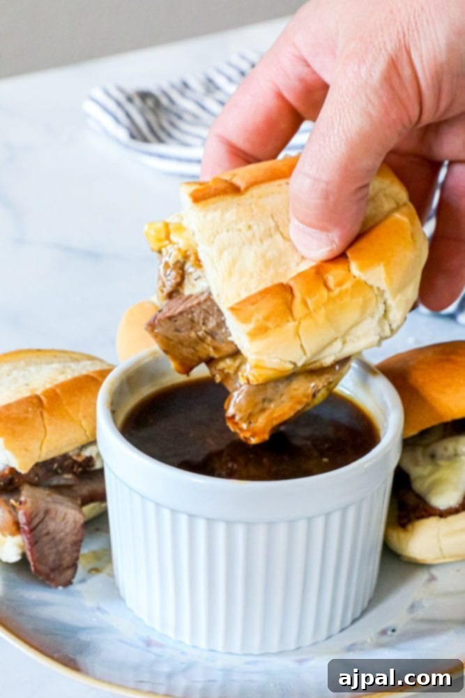Photo of hand dipping french dip sandwich into pot of au jus sauce