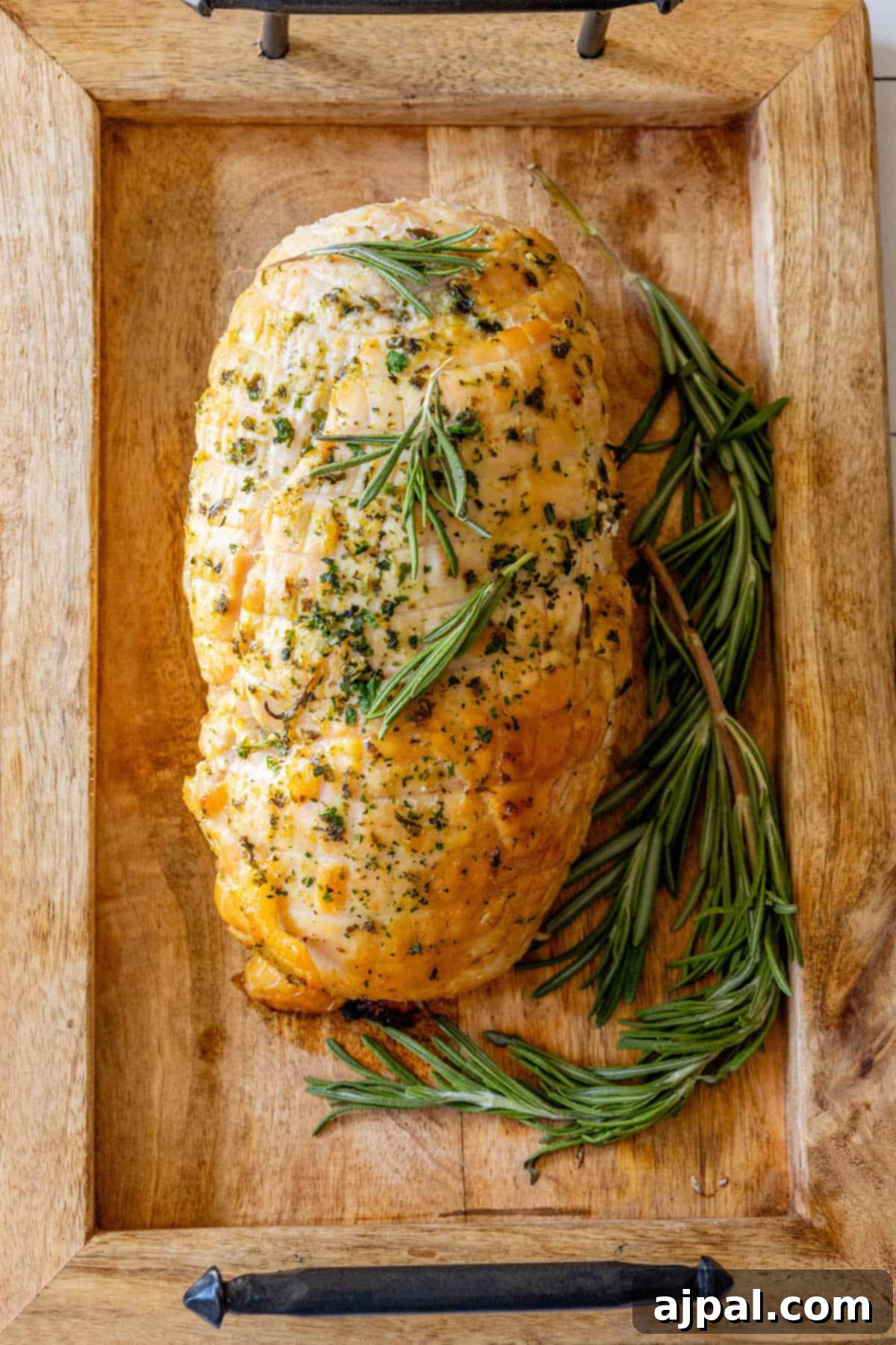 Perfectly Juicy Oven Roasted Turkey Breast 4 An Oven Baked Turkey Breast with rosemary on a wooden tray.