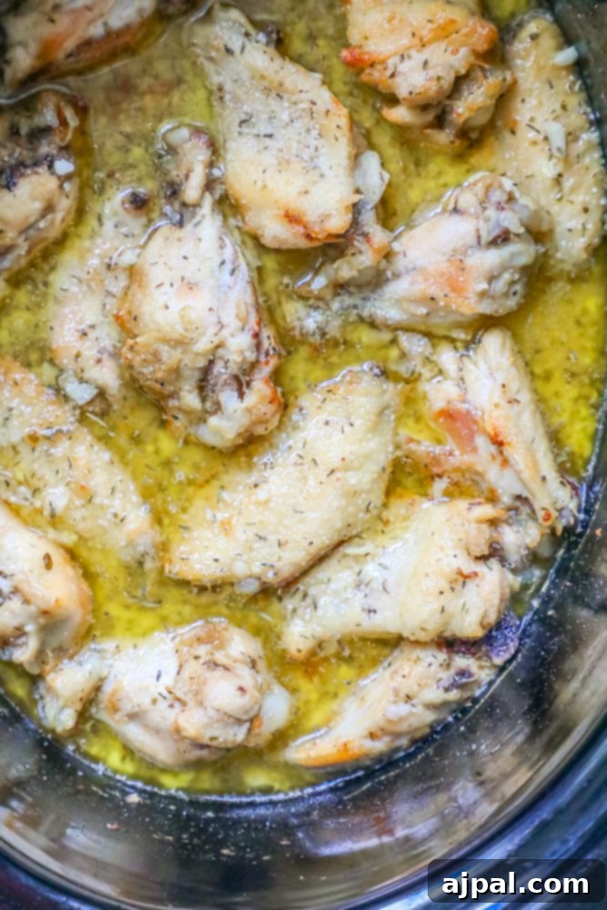 Parmesan chicken wings cooking in a slow cooker, bubbling in a rich sauce.