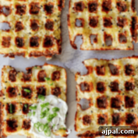 Ultimate Keto Chaffles 7 Sliced keto chaffles topped with melted cheese and bacon bits, served with a dollop of sour cream and garnished with chopped green onions.