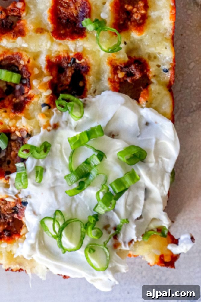Ultimate Keto Chaffles 4 Close-up of golden-brown keto chaffle waffles, one topped with a dollop of sour cream and a sprinkle of fresh green onions