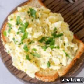 A slice of bread topped with creamy egg salad, from The Best Classic Egg Salad Recipe, garnished with chopped parsley and a sprinkle of ground black pepper.