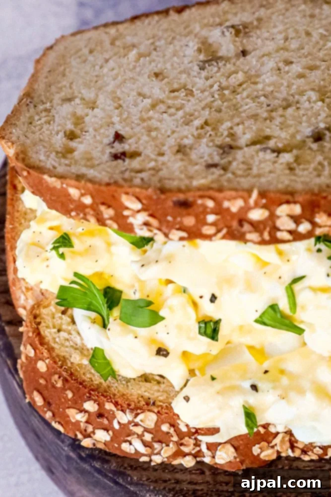 An easy and flavorful egg salad sandwich, garnished with fresh herbs, presented on a simple white plate.