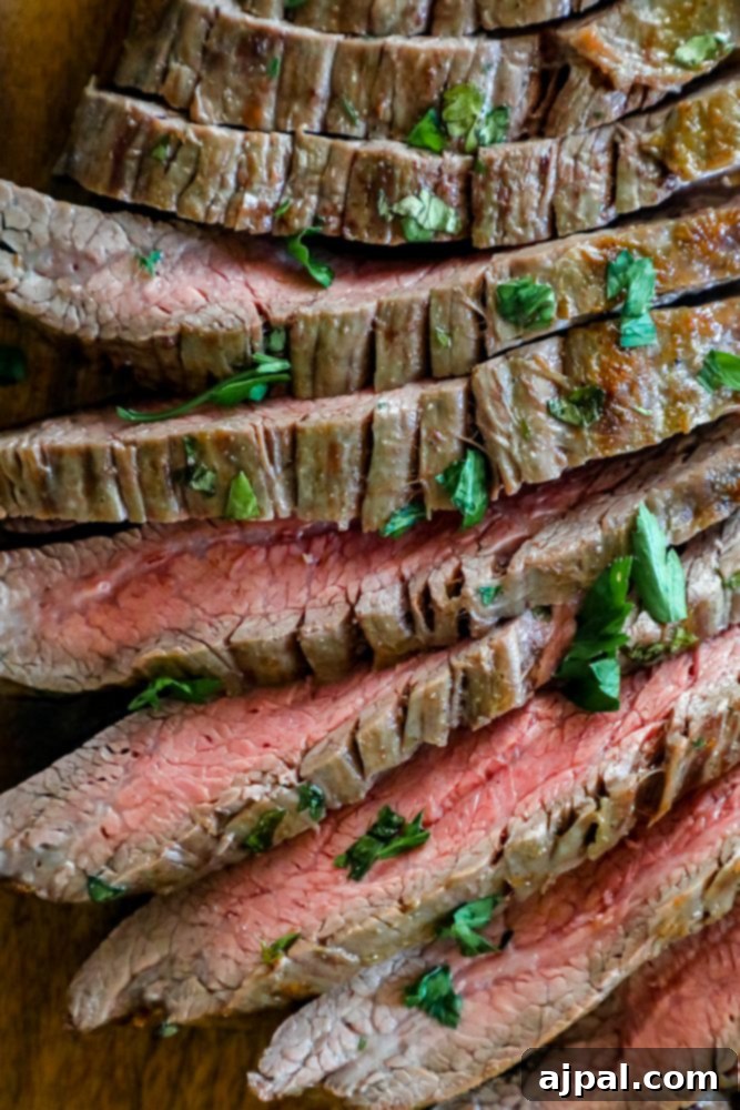 Perfectly Tender Oven Flank Steak 3 Steak with herbs on a cutting board prepared with a garlic butter roasted flank steak recipe.
