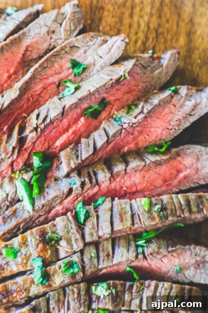 Perfectly Tender Oven Flank Steak 4 Sliced steak on a cutting board with herbs, garlic butter roasted flank steak recipe.