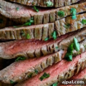 Steak with herbs on a cutting board prepared with a garlic butter roasted flank steak recipe.