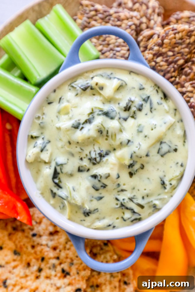 A beautifully presented bowl of creamy spinach and artichoke dip, surrounded by an assortment of crackers, colorful bell peppers, and crisp celery sticks, perfect for a gathering.
