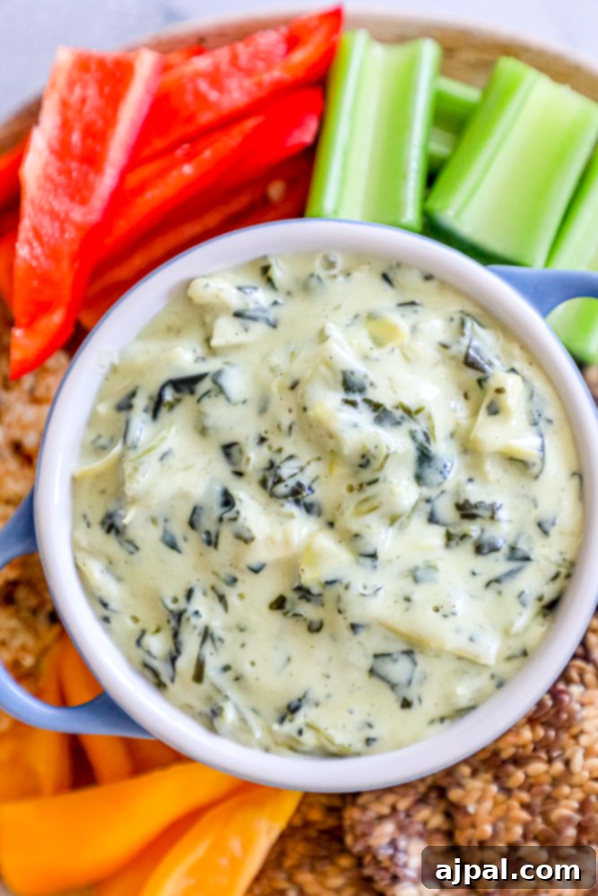 A vibrant bowl of spinach and artichoke dip, encircled by a colorful selection of fresh vegetables and crispy crackers, showcasing the perfect presentation for The Best Easy Spinach and Artichoke Dip Recipe.