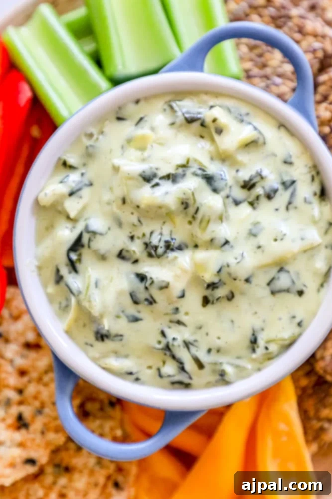 A beautifully arranged low-carb spinach and artichoke dip, accompanied by an assortment of crisp keto crackers and fresh celery, showcasing a healthy and delicious appetizer option.