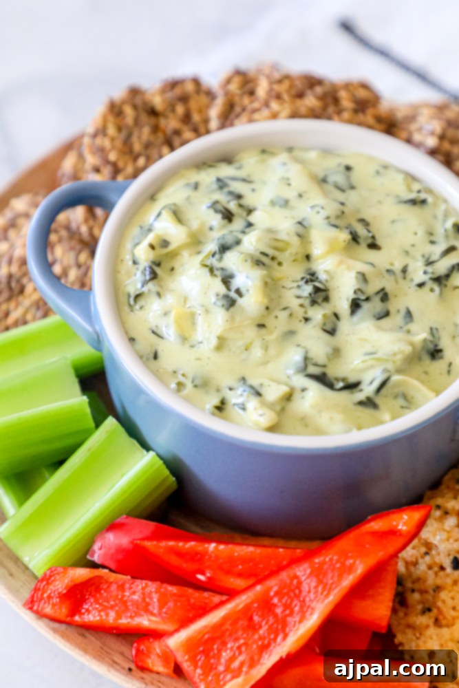 A inviting bowl of keto spinach and artichoke dip, accompanied by an array of crisp crackers and fresh celery sticks, perfect for a healthy and satisfying snack or appetizer.
