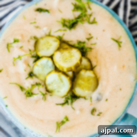 A close-up of a creamy pickle soup garnished with sliced pickles and chopped fresh herbs in a blue bowl—a delicious twist on the classic dill pickle soup recipe.