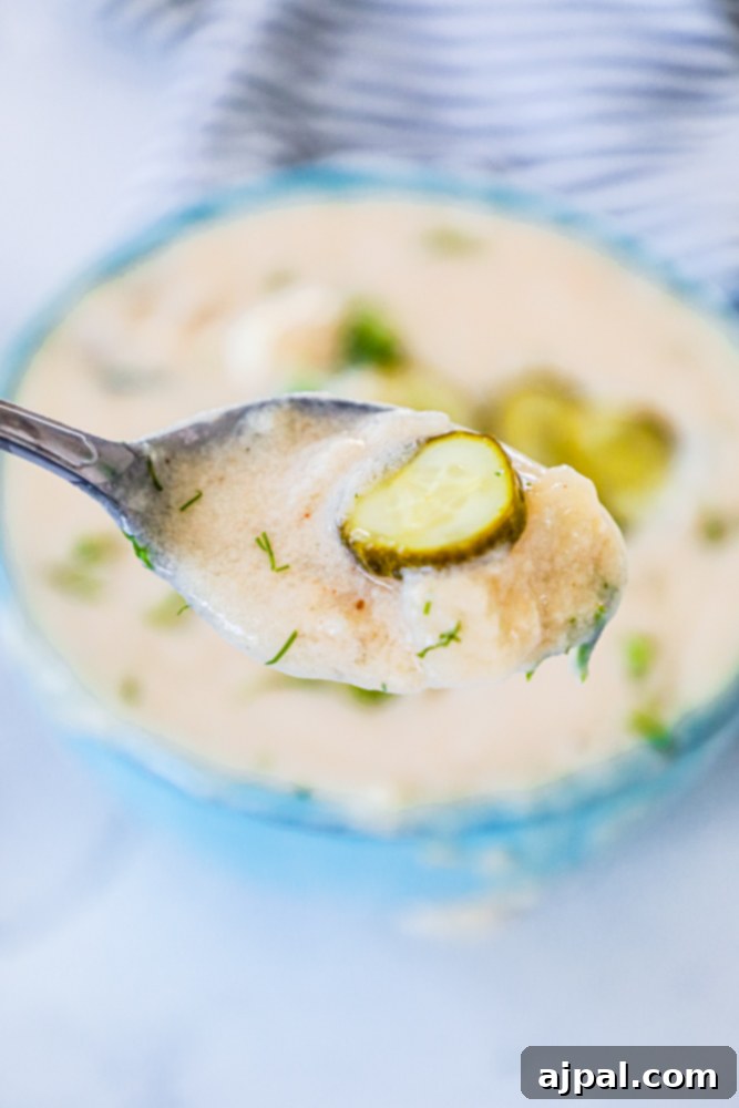 Simple Dill Pickle Soup 5 A close-up view of creamy dill pickle soup with pickle slices visible, ready to be served in a rustic bowl.
