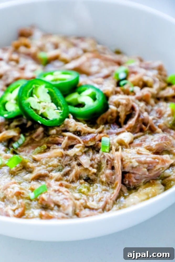 Zesty Green Chile Pork Carnitas 2 A vibrant bowl of shredded green chile pork carnitas, garnished with fresh jalapeños and green chiles.