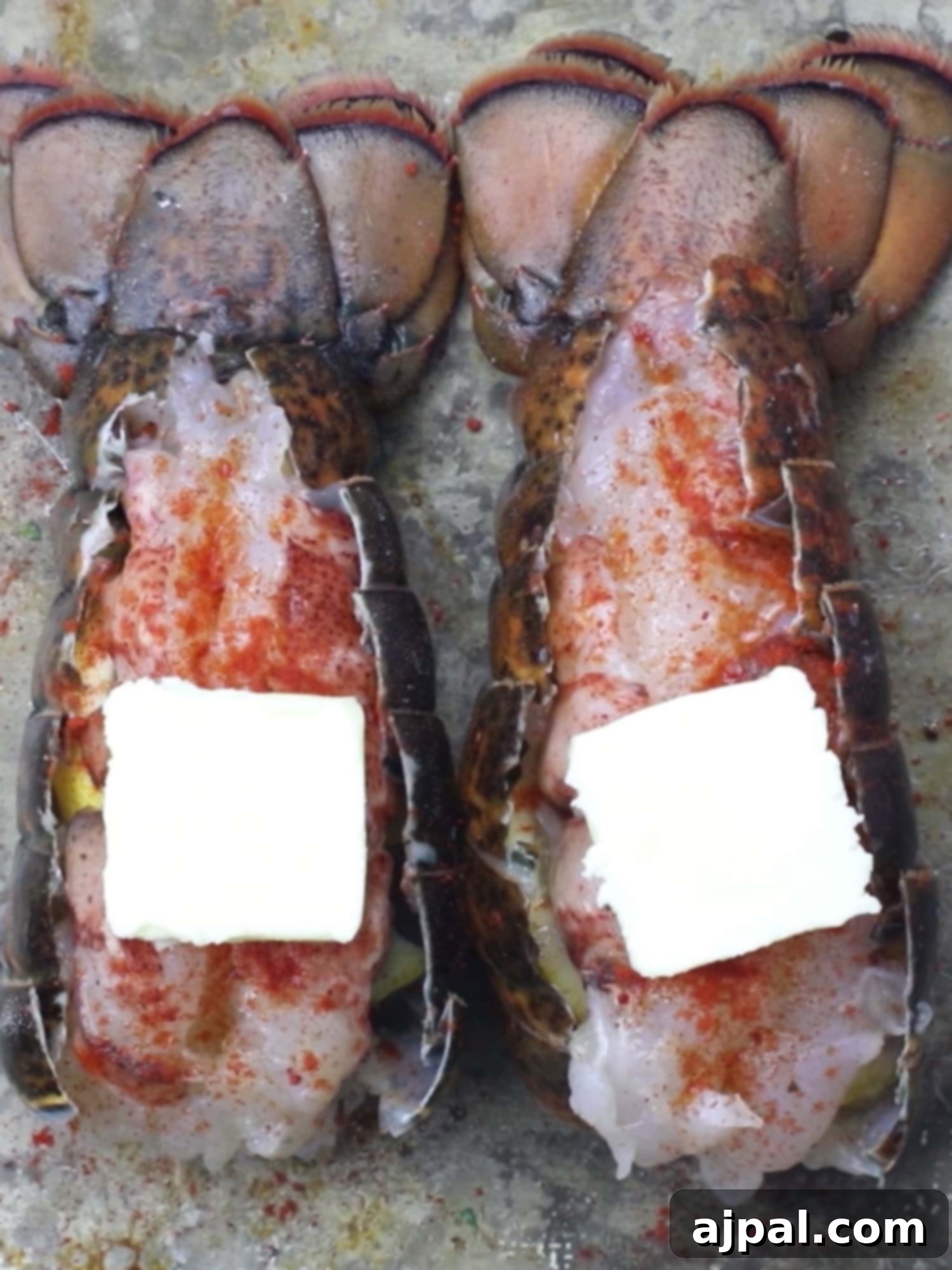Raw lobster tail generously seasoned with paprika and dotted with butter pats.