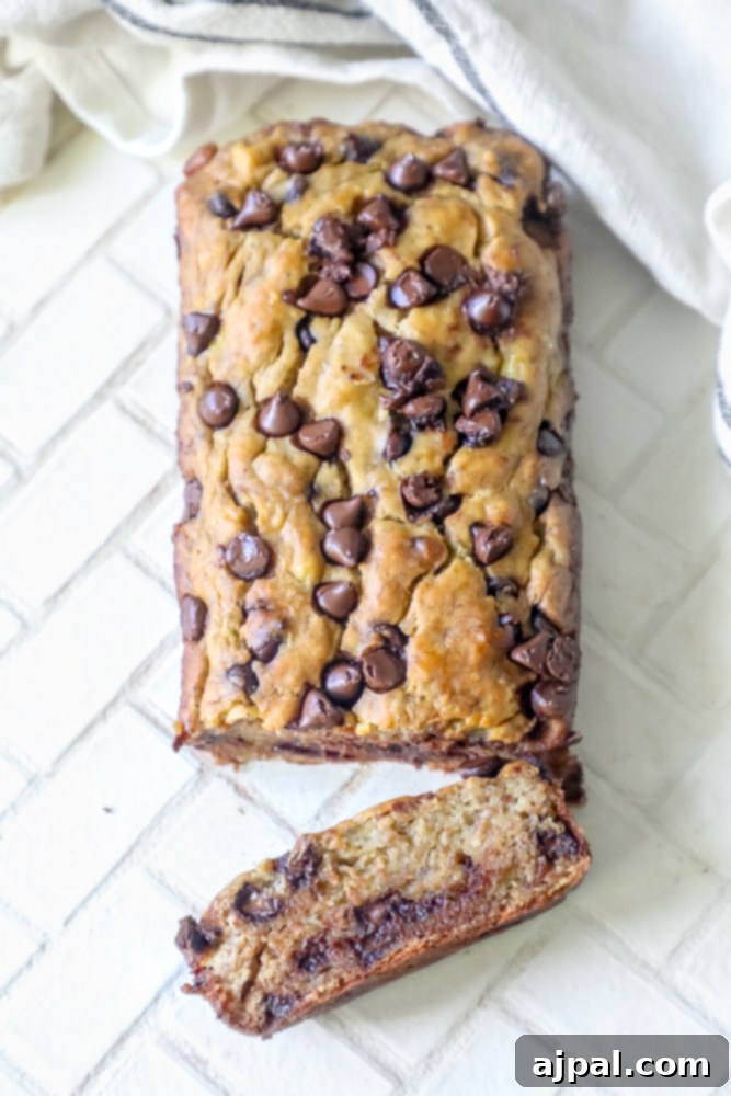 A beautiful loaf of chocolate chip banana bread on a cutting board with a slice cut off, ready to serve