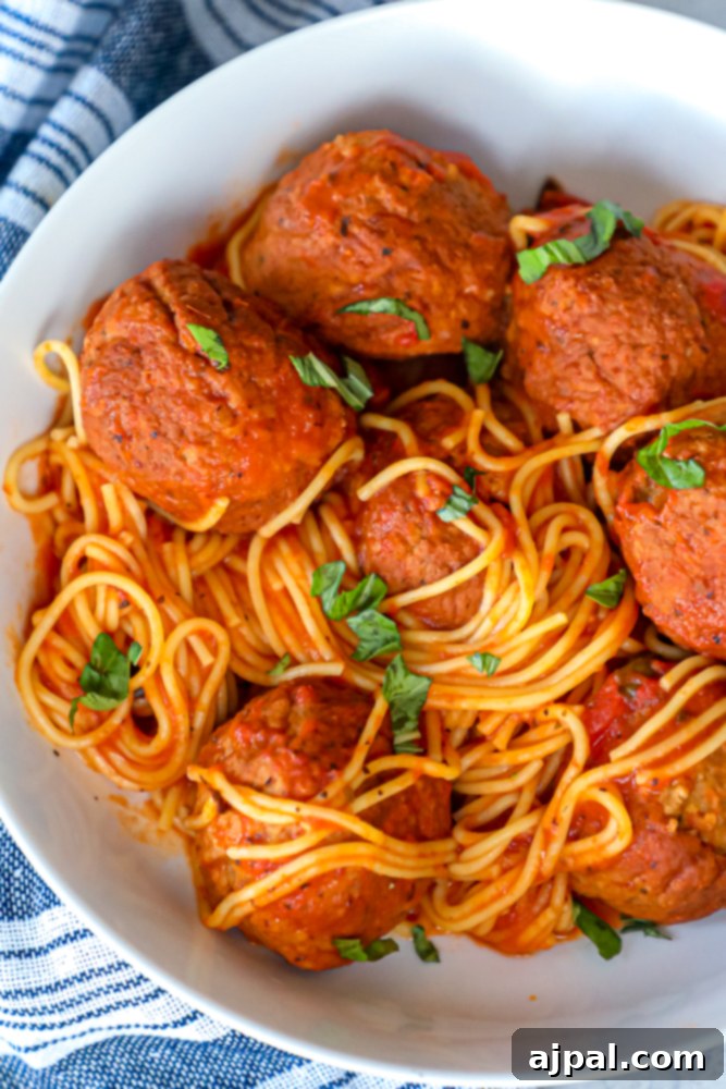 Picture of spaghetti and meatballs in bowl, garnished with fresh herbs