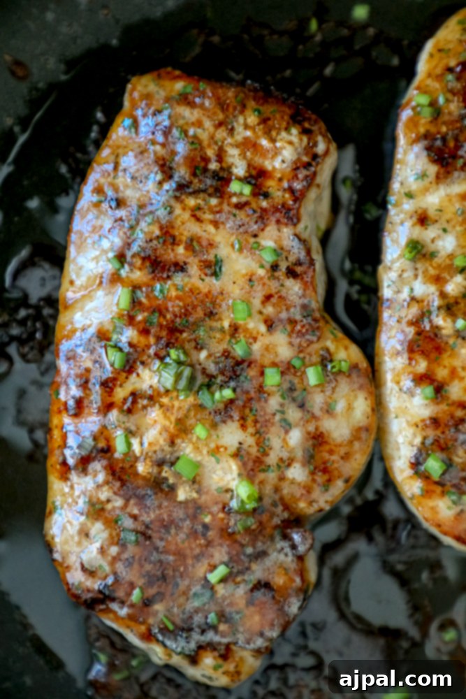 Two perfectly seared ranch pork chops, sprinkled with chives, cooking in a skillet.