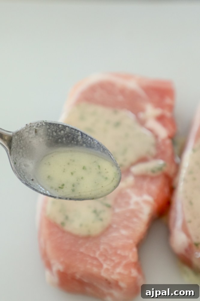 Spoon drizzling a savory ranch marinade over raw pork chops on a white plate.