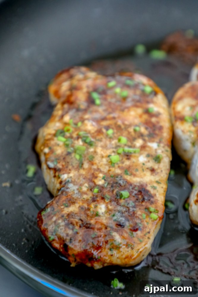 A baked ranch pork chop, topped with fresh minced chives, resting in a skillet.