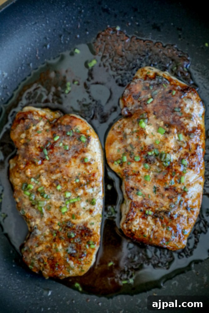 Two easy baked ranch pork chops, garnished with fresh chives, in a frying pan.