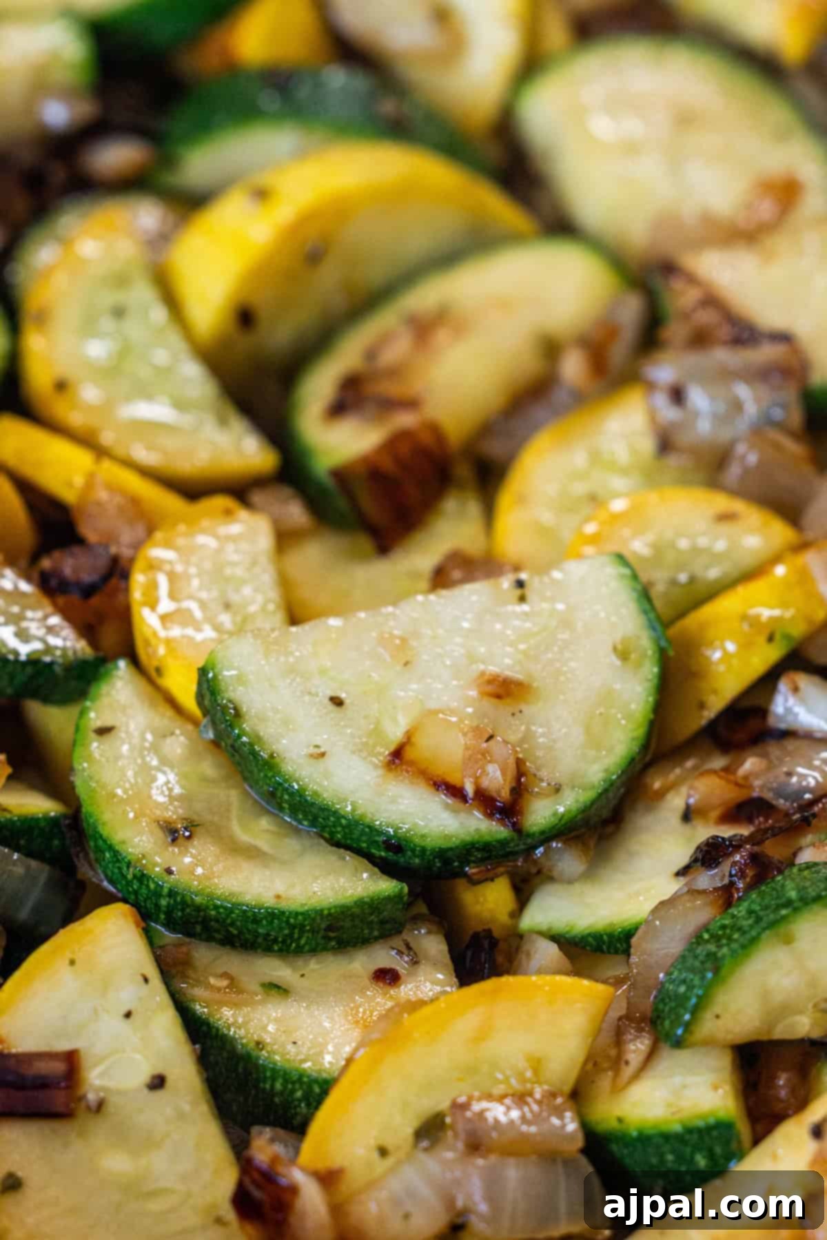 Close-up of sautéed zucchini and yellow squash slices with caramelized onions, seasoned with salt, pepper, and visible grill marks—a delicious zucchini and squash side dish perfect for any meal.