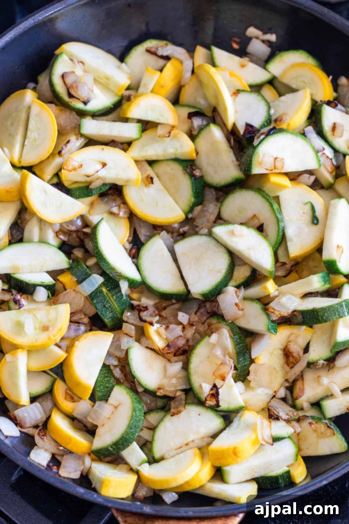 Sliced zucchini and yellow squash with chopped onions sautee in a black skillet for a tasty zucchini and squash side dish.