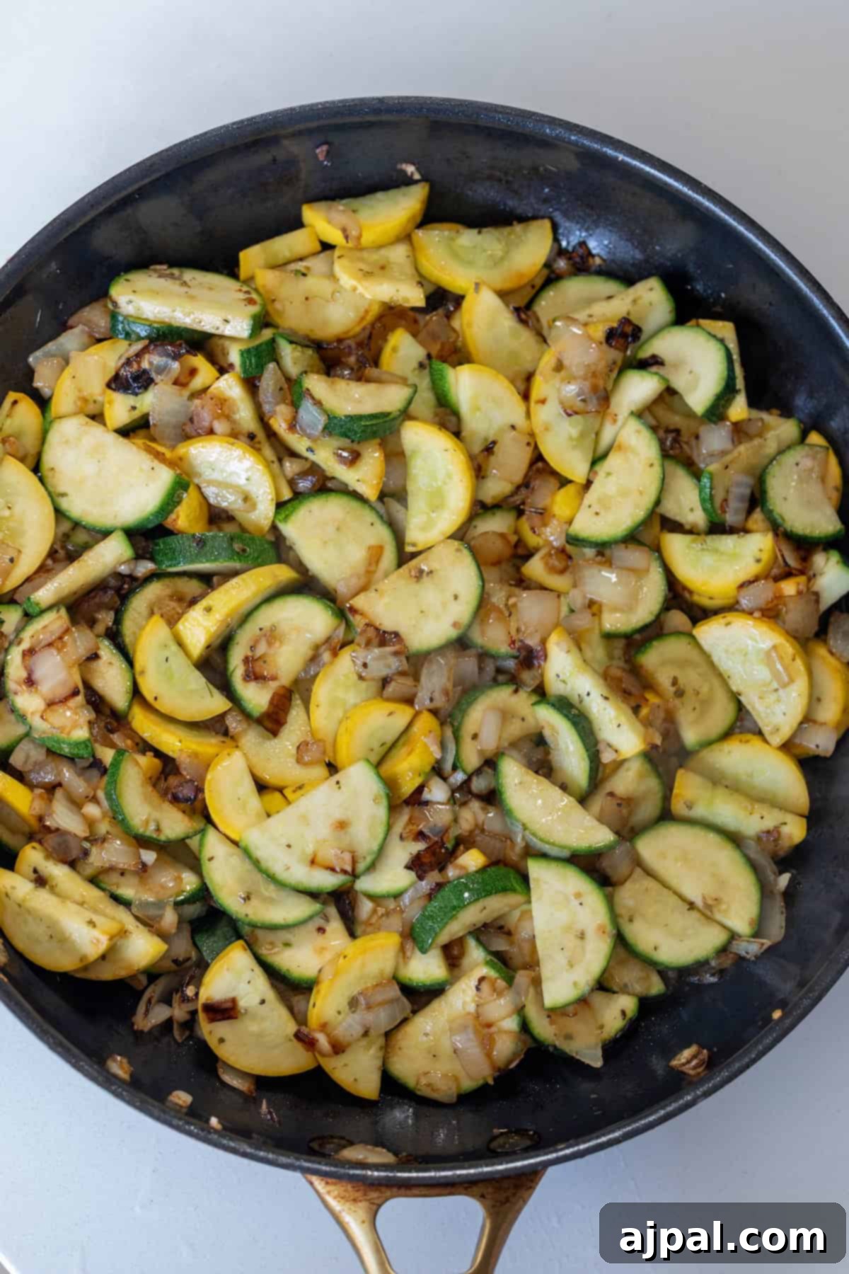 Sautéed sliced yellow squash, zucchini, and diced onions in a black skillet for a flavorful zucchini and squash side dish.