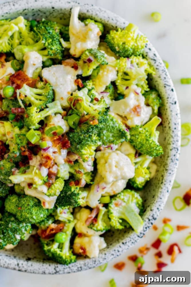 creamy dressed broccoli and cauliflower in a bowl with diced bacon and onions
