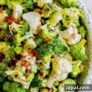 picture of broccoli and cauliflower salad in a speckled bowl with bacon and peas