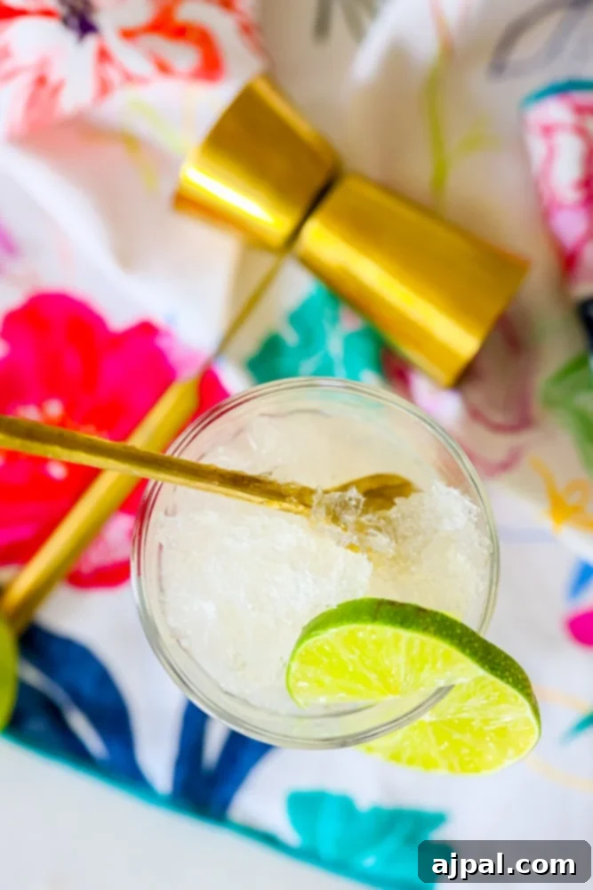A vibrant green frozen gin and tonic slush in a glass jar, garnished with fresh lime slices and a elegant gold spoon, perfect for a refreshing summer drink.