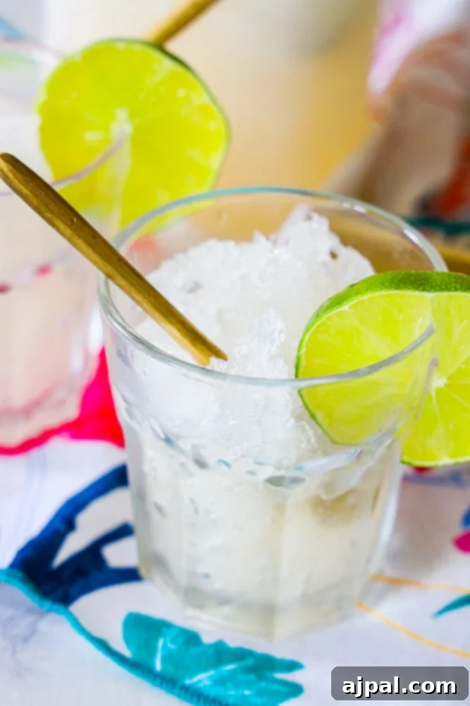 Two elegantly presented glasses with ice and fresh lime slices sit on a wooden table, featuring a delectable frozen gin and tonic slush, ready to be enjoyed.