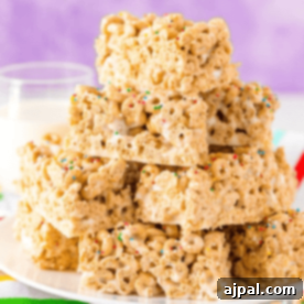 A stack of Cheerios bars dessert with colorful sprinkles sits on a plate against a purple backdrop, accompanied by a glass of milk in the background.