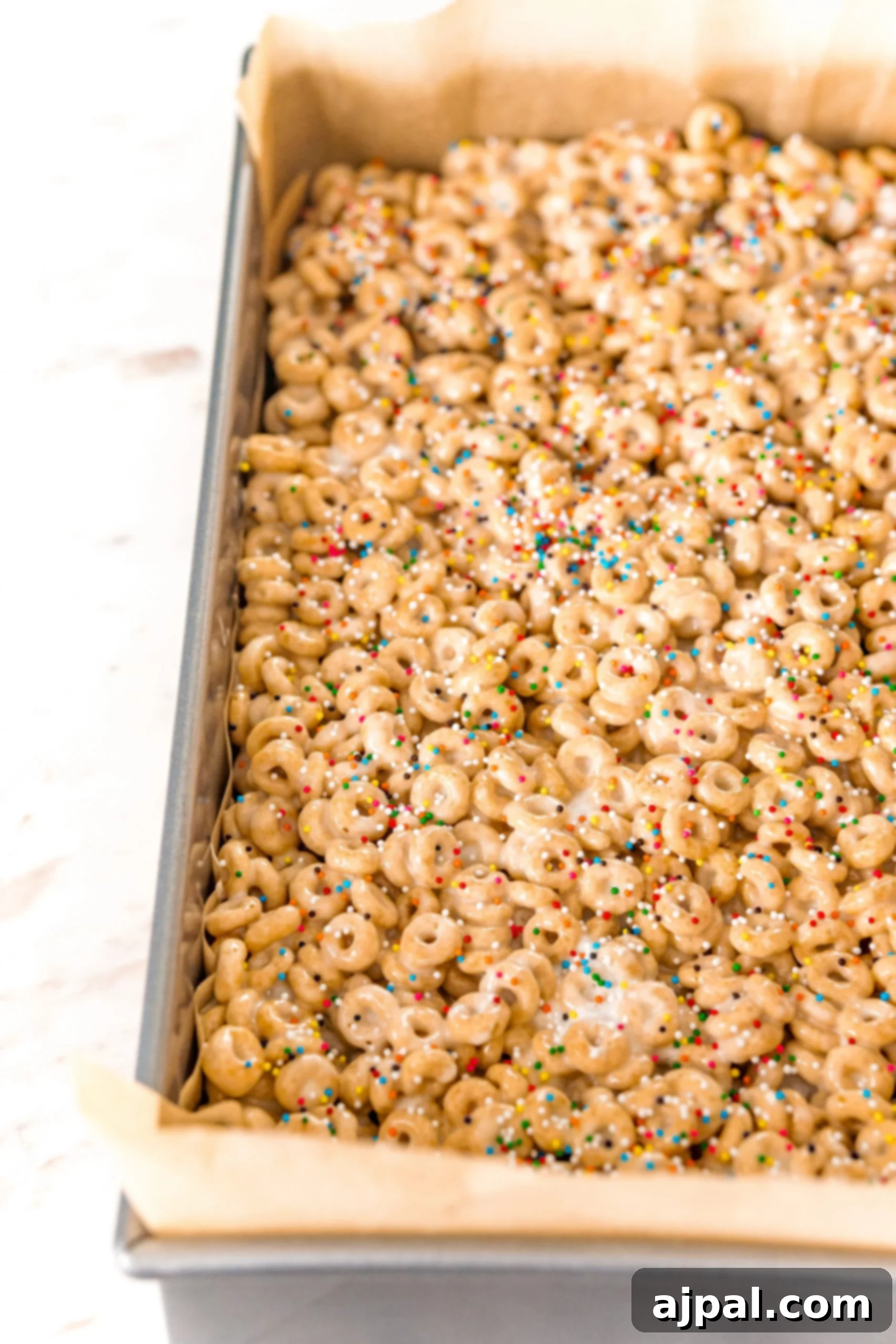 The freshly pressed Cheerio treats, adorned with colorful sprinkles, cooling in the baking pan, waiting to be cut.
