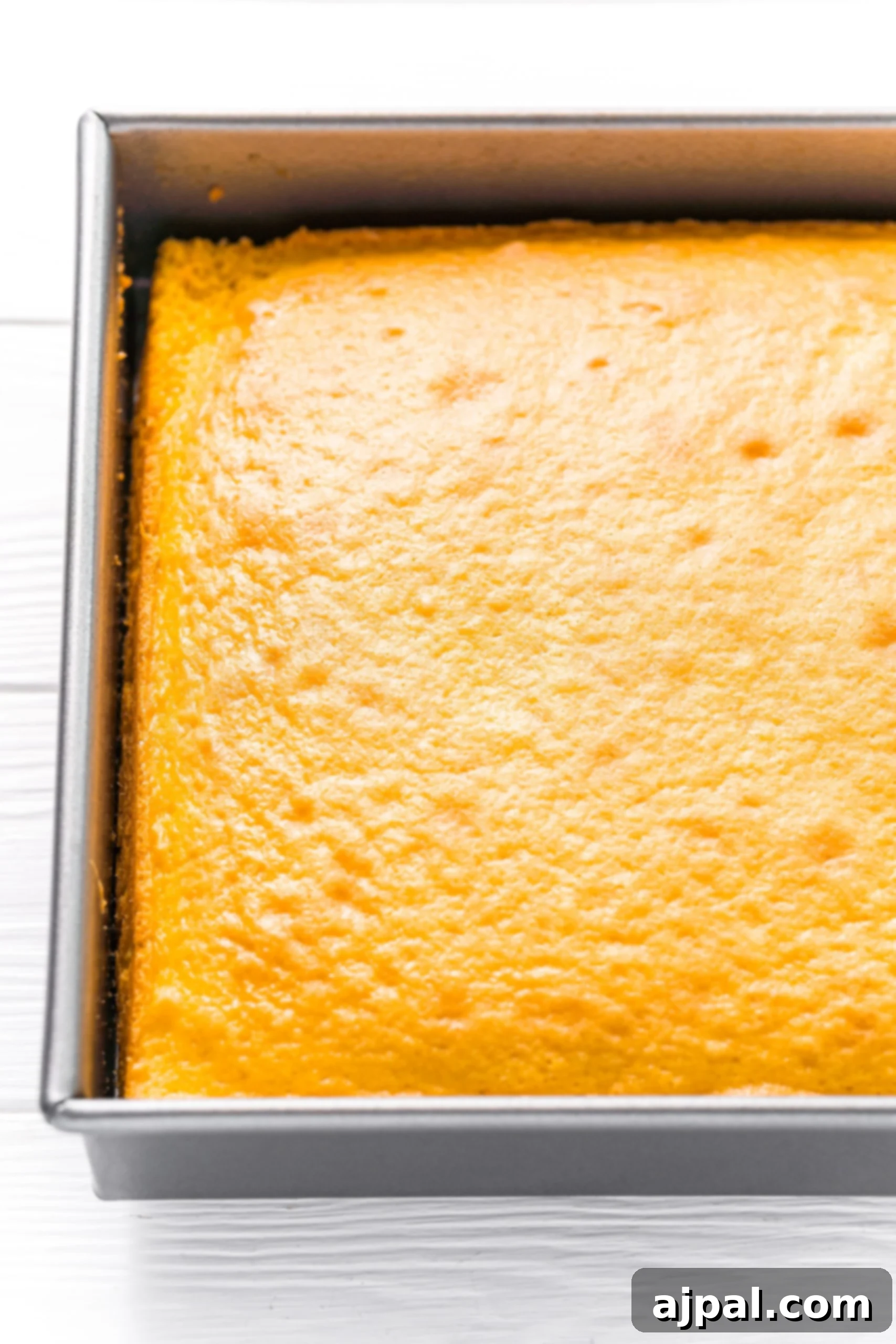Effortless Lemon Jello Poke Cake 4 Easy Lemon Jello Poke Cake Recipe with a square of cake in a pan on a white background.