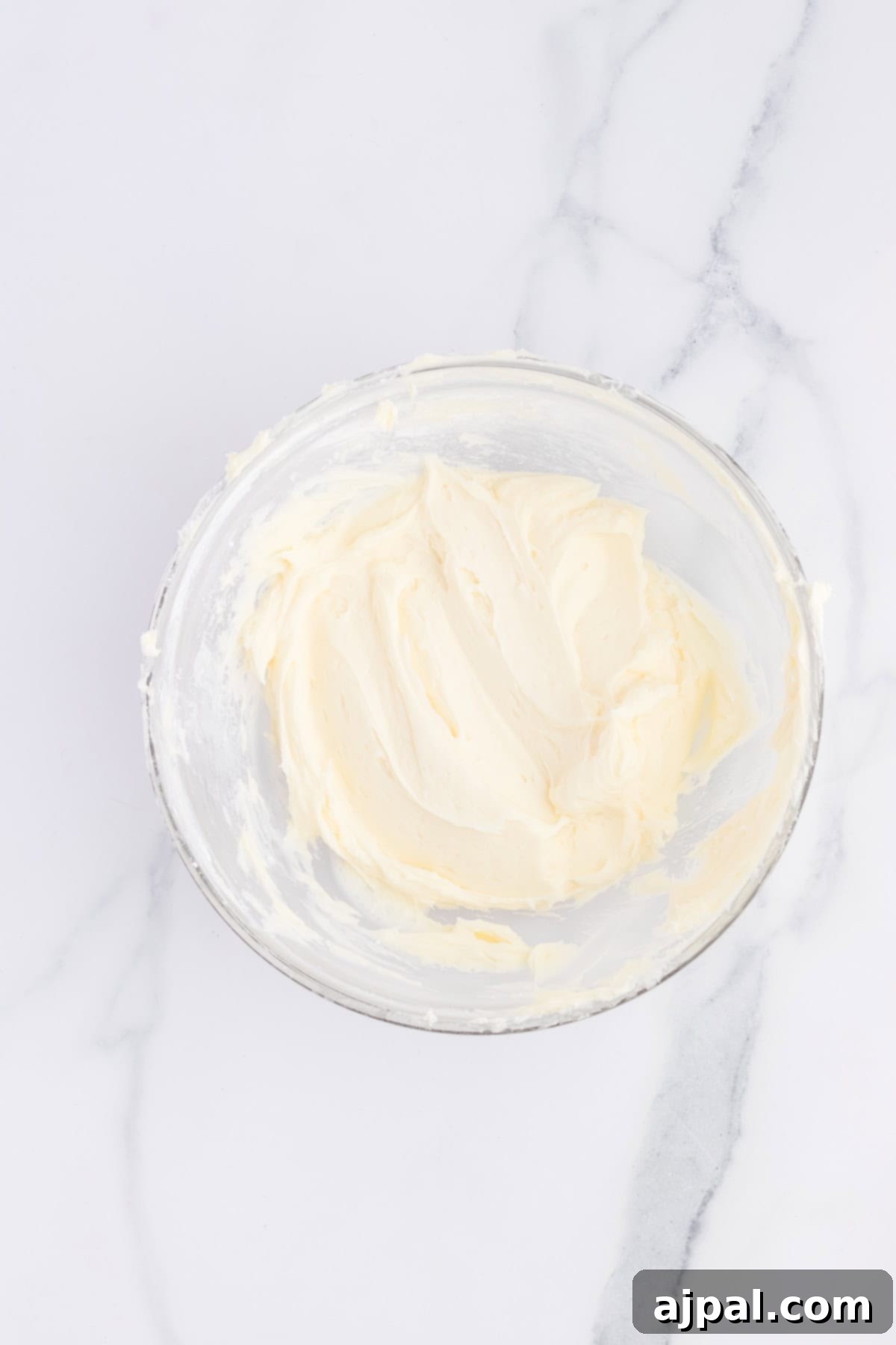Effortless Lemon Jello Poke Cake 7 A bowl of creamy, smooth frosting sits on a marble countertop, perfectly primed for decorating your favorite cupcakes.