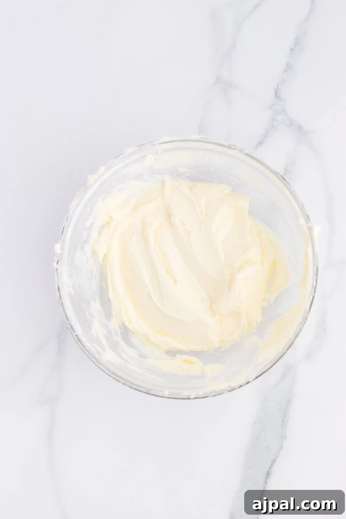 A large bowl filled with creamy, smooth, and fluffy lemon pudding frosting, perfectly whipped and ready to be spread over a cake.