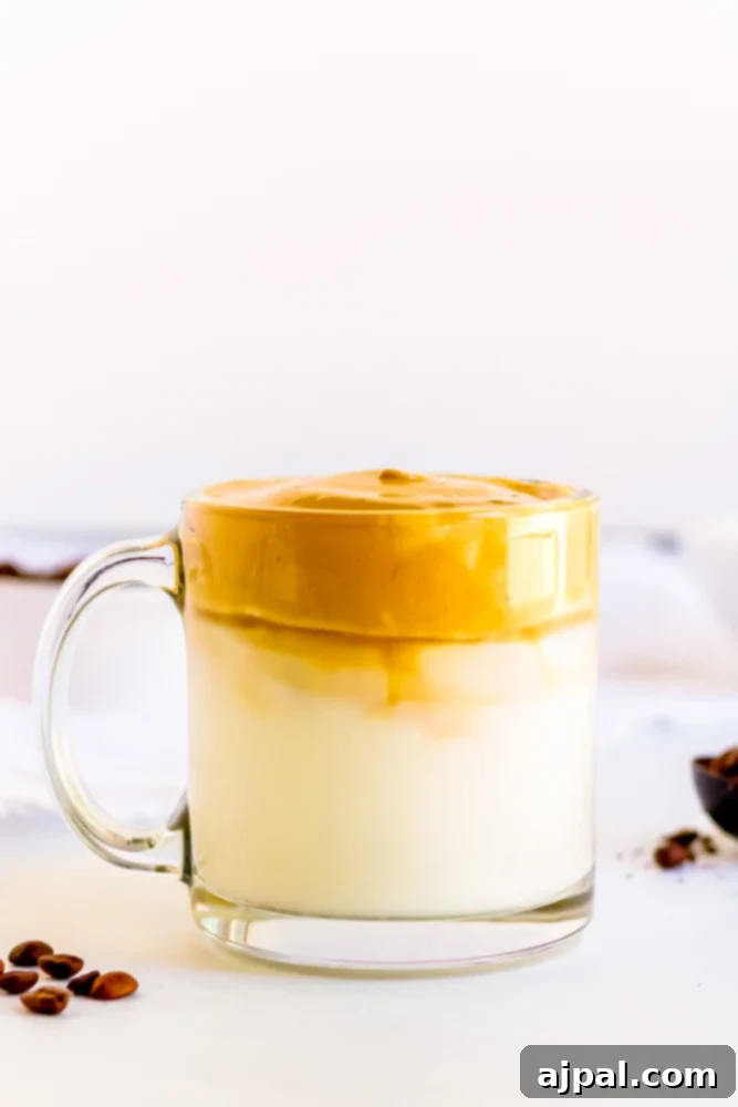 Close-up of a glass of creamy coffee with caramel-colored foam and whole coffee beans on the table.