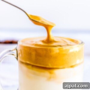 A spoon is being used to drizzle peanut butter on a cup of milk in an Easy Keto Dalgona Coffee Recipe.