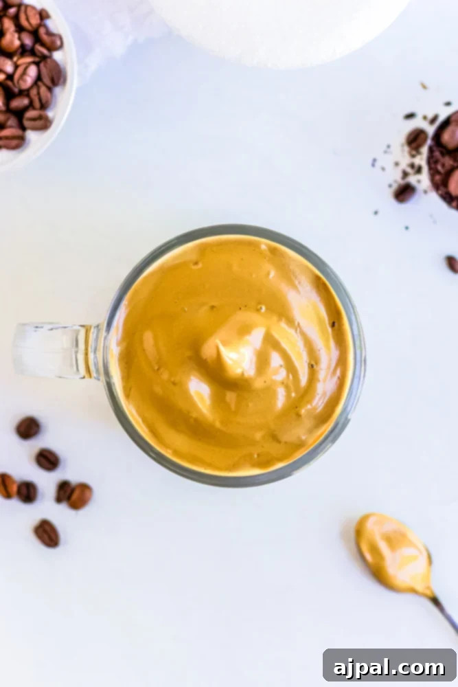 Keto Dalgona Coffee in a glass with a side of coffee beans and a jar of peanut butter.